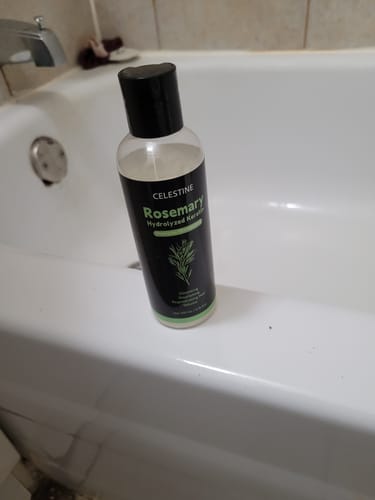 Customer's bottle of Natural Rosemary and Keratin Shampoo sitting on the edge of a white bathtub.