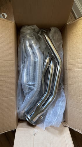 Customer's shiny new Exhaust Header in an open cardboard box, partially covered in bubble wrap.
