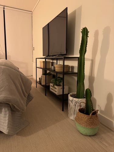 Reseña de un cliente del arrimo Kume METAL negro en un dormitorio, utilizado como soporte de TV con plantas y cajas decorativas.