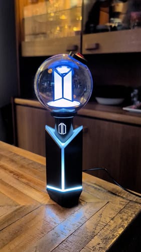 Customer's BTS Official Light Stick Ver.4 lit up in its glowing cradle on a wooden table.