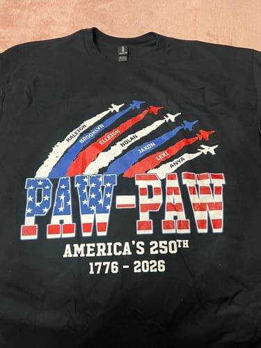 Customer's personalized black shirt with 'Paw-Paw' in an American flag design and custom names in patriotic jet trails.