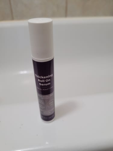 A customer's bottle of SÉRUM NATUREL AU ROMARIN standing upright on the white ledge of a bathtub.