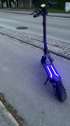 Kunde zeigt seinen Ausom L2 Max E-Scooter mit leuchtenden blauen LEDs auf einem Bürgersteig.