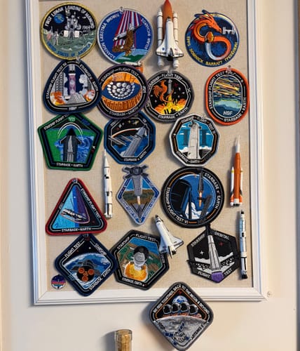 Customer's large collection of space-themed patches, including the Starship Flight 12 patch, displayed on a board.