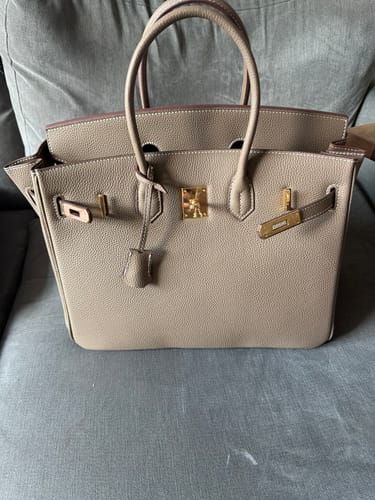Customer's structured beige LALUVA Warkin Bag with gold hardware, shown sitting on a grey fabric couch.