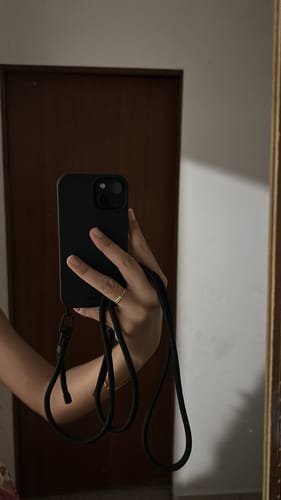 Cliente segurando um celular com a Case preta e sua alça.