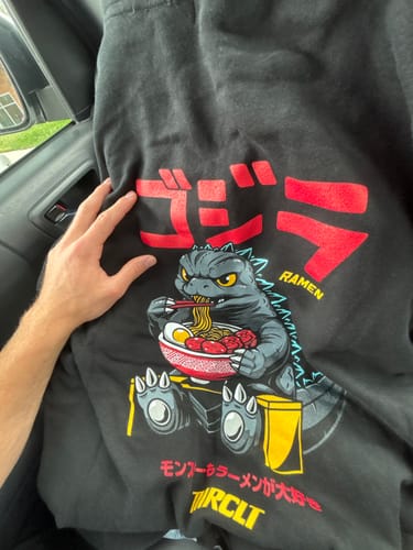 A customer holding up their black RAMEN MONSTER HOODIE to show the front graphic of a monster eating ramen.