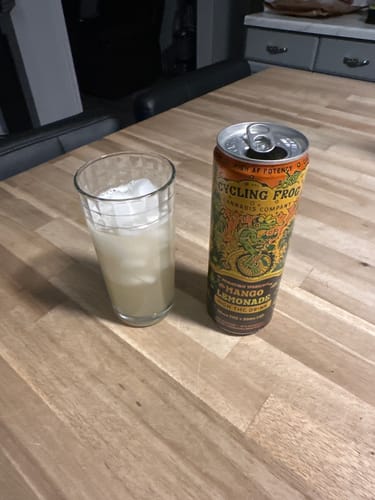 Reviewer's can of Sparkling THC Mango Lemonade on a table next to a glass of the drink with ice.