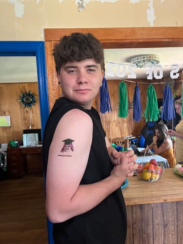 Customer at a party showing a custom graduation tattoo on their upper arm.