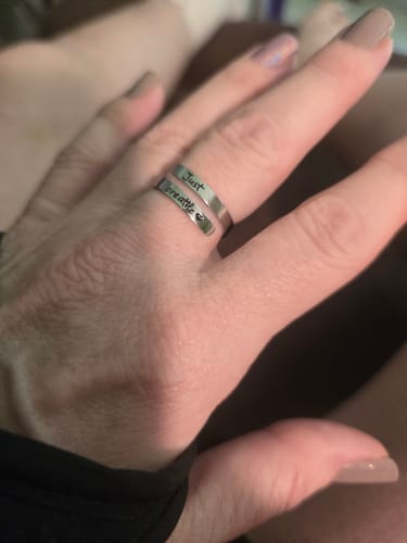 A customer's close-up of the adjustable Just Breathe Ring on their finger, showing the engraved text.