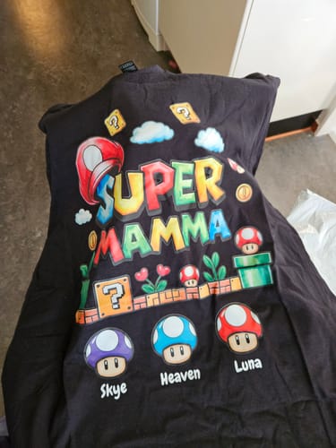 Ein Kunde zeigt sein personalisiertes schwarzes „Super Mamma“-T-Shirt mit den Namen Skye, Heaven und Luna.