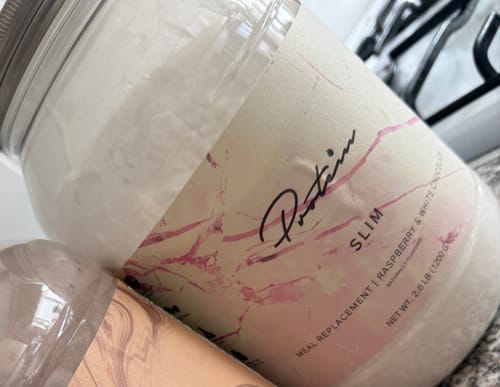 Customer's close-up of a large jar of Slim Meal Replacement powder, showing the Raspberry & White Chocolate flavor label.