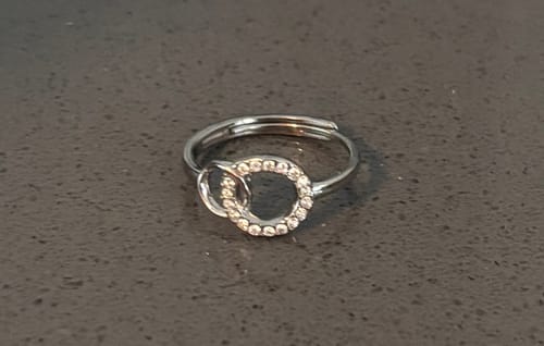 Reviewer's photo of the incorrect ring received; a silver-colored adjustable ring with two interlocking circles, one paved with stones.