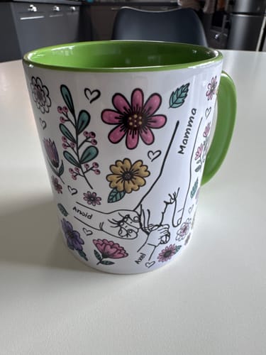 Kundens Kärleksmugg med grön insida, med ett personligt tryck av händer, blommor och namnen Mamma, Arnold och Axel.