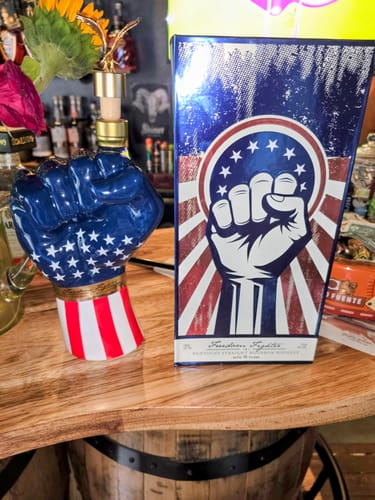 Customer's Freedom Fighter Bourbon bottle, shaped like a patriotic fist, beside its box on a wooden table.