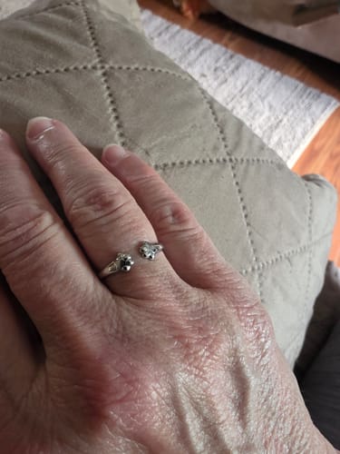 A customer's hand wearing the silver Paw Hug Ring on their finger against a cushioned background.