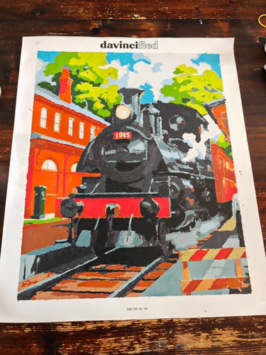 A customer's completed paint-by-numbers canvas of a black steam train at a colorful brick station.