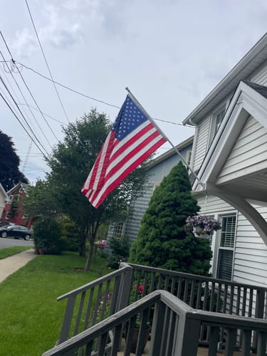Customer's durable American nylon flag waving from a pole on the front of their home.
