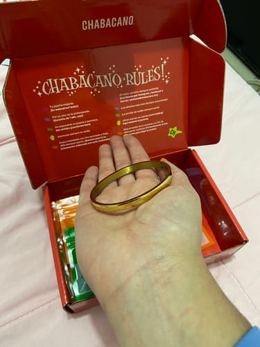 Cliente sosteniendo la Pulsera Elizabeth dorada en la palma de su mano, sobre la caja del producto.
