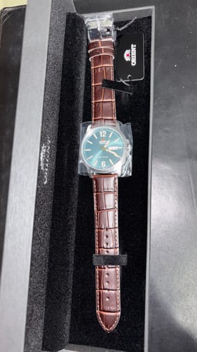 Reseñador mostrando el reloj Orient Commuter con esfera verde y correa de cuero marrón en su caja.