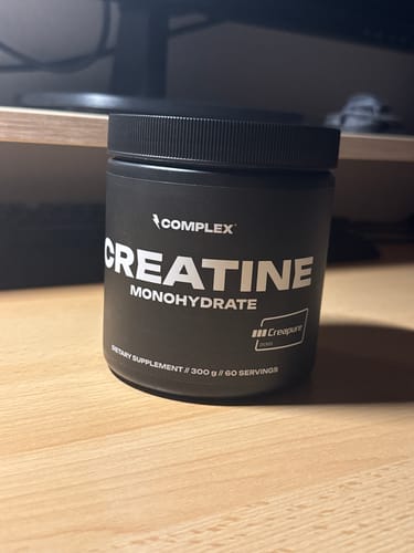 Customer's black tub of Complex Creatine Monohydrate sitting on a wooden desk.