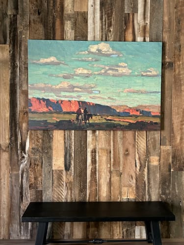 Customer's Riders Under Scattered Clouds canvas hanging on a rustic wood-paneled wall above a bench.