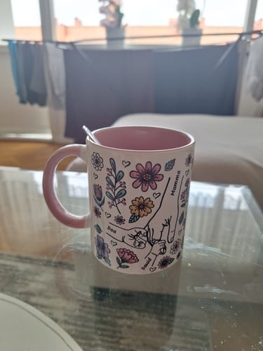 Kundens Kärleksmuggen med personligt tryck av händer och blommor, placerad på ett glasbord.