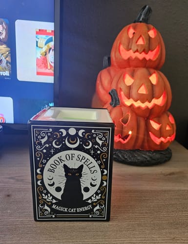 Kundenbewertung: Die Duftlampe mit „Book of Spells“-Design steht auf einem Tisch neben einer leuchtenden Kürbis-Deko.