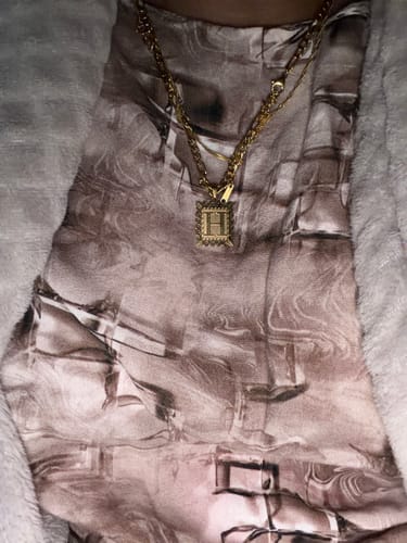 Close-up of a reviewer wearing the gold Embossed Initial Necklace with a square 'H' pendant.