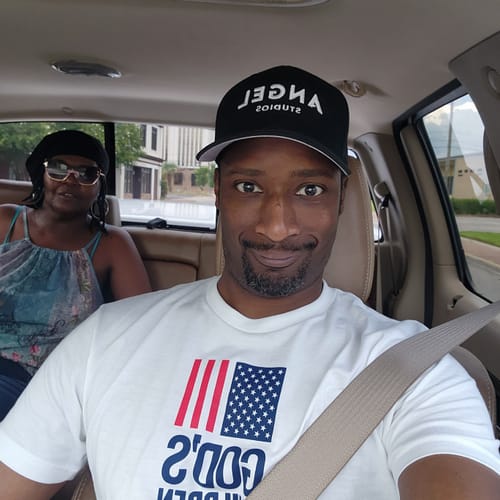 Customer smiling in a car while wearing the black Angel Studios Fitted Hat.