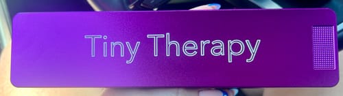 Close-up of a reviewer holding their purple metal Weekly Case, engraved with 'Tiny Therapy'.