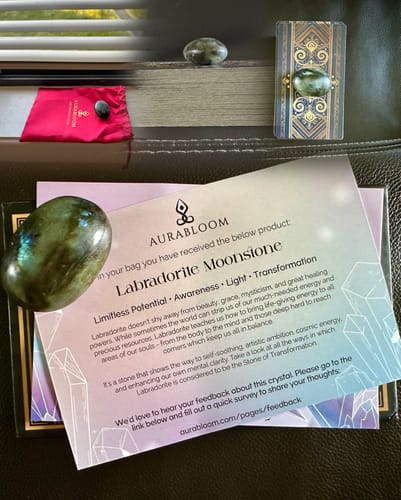 Reviewer's monthly crystal delivery showing a polished Labradorite Moonstone, its info card, and a storage pouch.