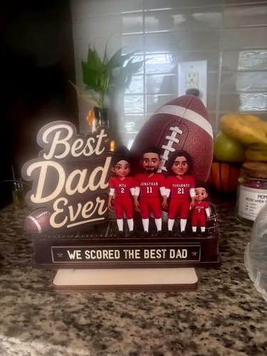 Customer's personalized wooden football plaque with figures of a dad and three children in red jerseys on a kitchen counter.
