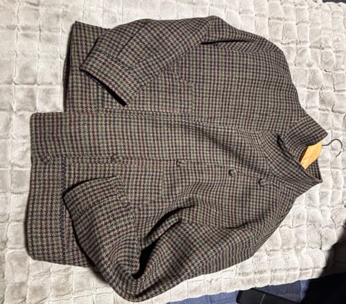 Cliente muestra la Chaqueta Delfina gris con patrón de cuadros, extendida sobre una superficie texturizada.