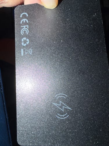 Reviewer holding the back of the black, card-shaped SmartTag, showing the wireless charging symbol.