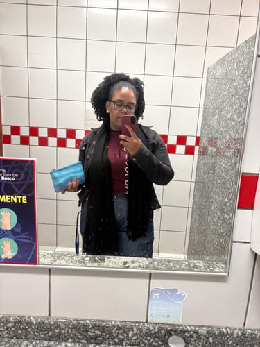 Cliente tirando uma selfie no espelho, mostrando o uso da Cordinha Odara bordô para segurar seu celular.