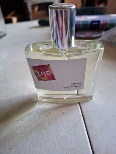 Reviewer's bottle of For Her Pheromone Perfume, showing the clear glass bottle and silver cap on a table.