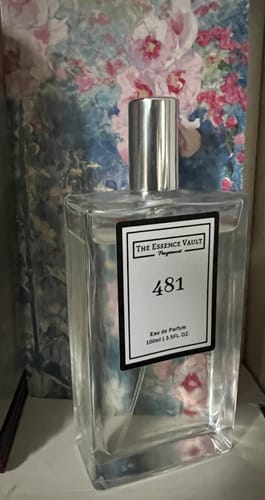Reviewer's clear glass bottle of 481 fragrance with a silver cap, set against a floral background.