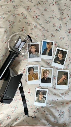 Customer's BTS Official Light Stick Ver. 4 and cradle, arranged with seven member photocards on a floral surface.