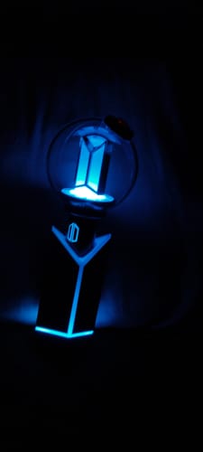 Customer's BTS Official Light Stick Ver.4 lit up with a vibrant blue light in a dark room.
