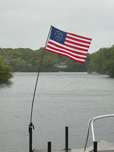 Customer's 1776 to 2026 Betsy Ross Flag flying on a pole from a dock over the water on an overcast day.