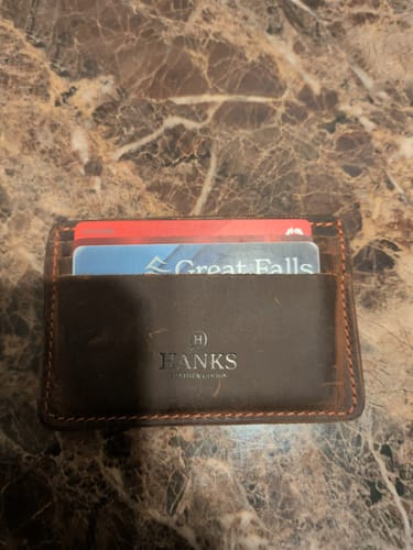 Customer's dark brown leather Hamlin Card Holder with several cards inserted, on a marbled countertop.