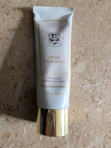 Customer's white tube of Crème d'Albarosa Brightening Cream with a reflective gold cap on a counter.