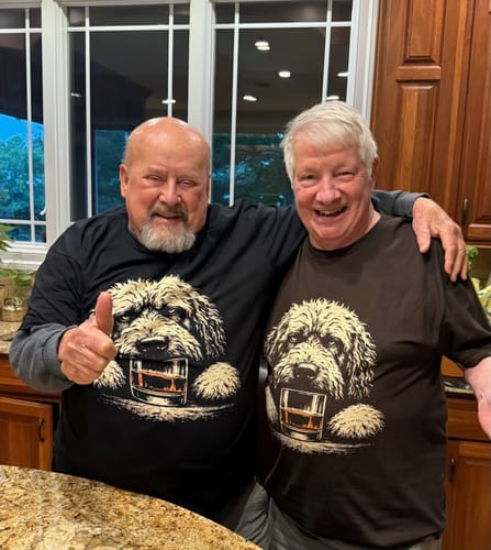 Two smiling customers posing together in a kitchen, both wearing the Whiskey Dog Cavalier King Charles Spaniel T-Shirt.
