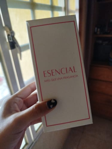 Una clienta sostiene la caja del perfume ESENCIAL frente a una ventana.