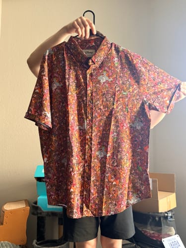 A reviewer holds up the colorful, patterned Disney's The Jungle Book "Monkey Business" shirt on a hanger.