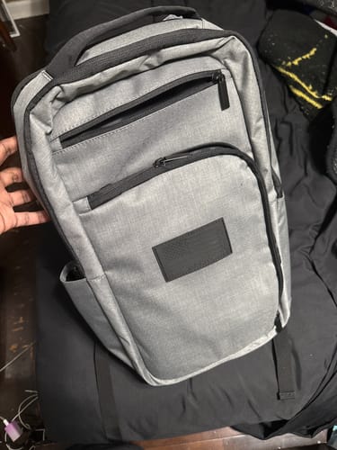 Customer's grey Impact Backpack with black zippers and a handle, resting on a bed.