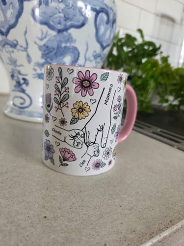 Kundens personliga Kärleksmugg med rosa handtag. Den visar en teckning av händer, blommor och namn.