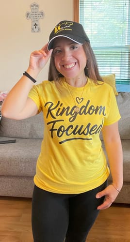 Reviewer smiling in a bright yellow Kingdom Focused t-shirt, showing a fitted style indoors.