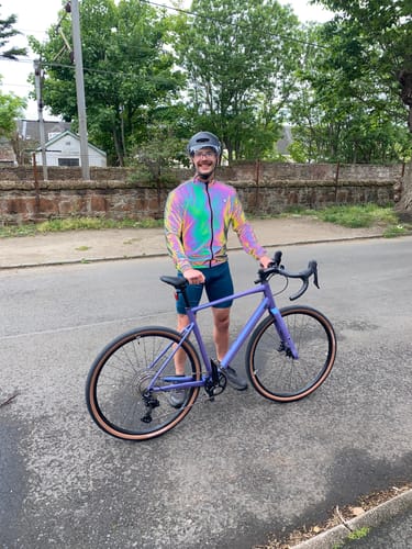 Reviewer outdoors with a bike, wearing the iridescent and reflective GLOWMOTION JACKET.